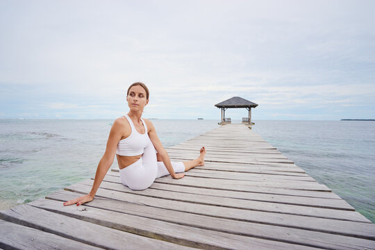 Yoga on the beach. Young woman stretching on wooden pier with sea view.