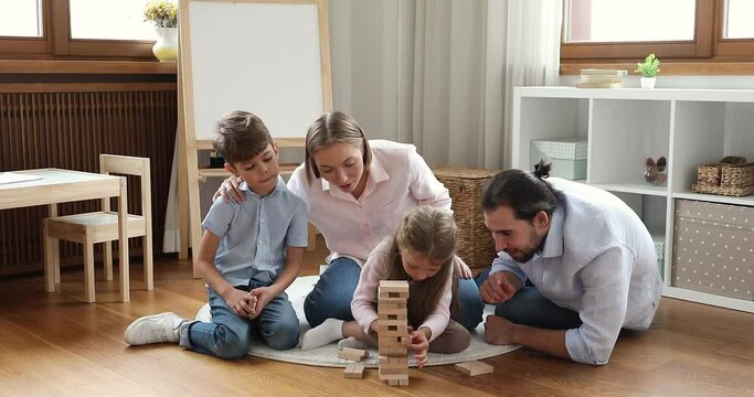 Young couple and siblings play game sit on floor in playroom. Little boy and girl spend weekend leisure with loving parents enjoy wooden tumbling tower boardgame. Family fun, kids development concept