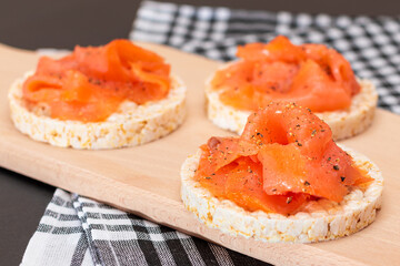 Tasty Rice Cake Sandwiches with Fresh Salmon Slices on Wooden Cutting Board. Easy Breakfast and Diet Food. Crispbread with Red Fish. Healthy Dietary Snack