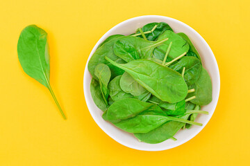 Fresh Baby Spinach Leaves in White Bowl on Yellow Background - Top View. Vegan and Vegetarian Culture. Raw Food, Green Leaves. Healthy Diet