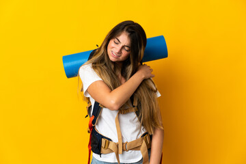 Young mountaineer woman with a big backpack isolated on yellow background suffering from pain in shoulder for having made an effort