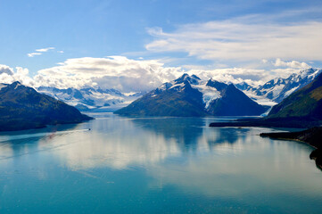 Fototapeta na wymiar Aerial shot of the stunning Prince William Sound. Mountains and glaciers surround the beautiful azure waters of the bay, a small boat speeds along in the distance. Kenai Peninsula, Alaska.