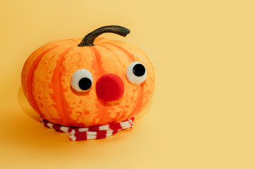 Funny pumpkin with eyes, nose and red scarf on yellow background