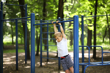 Fototapeta premium the boy goes in for sports in the park hung on the horizontal bar and sways