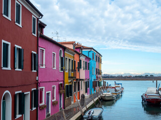 Fototapeta na wymiar A row of brightly colored houses face the canal on the beautiful Venetian island of Burano, the snow-capped Dolomite mountains are in the background - Burano, Venice, Italy