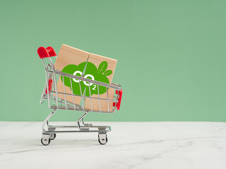Wooden cubes with CO2 green icons in a mini shopping trolley over a marble floor against a light green background - obrazy, fototapety, plakaty