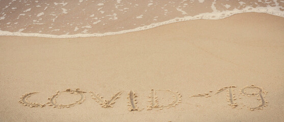 Inscription Covid-19 and incoming sea wave on sand at beach. Safe holidays