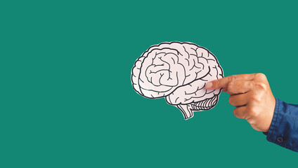 Close-up of hand holding a brain shape made from paper standing against a green background