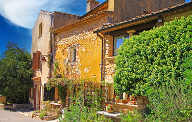 View on ochre natural stone farm house in provence style with lush green garden, blue sky - Roussillon, France