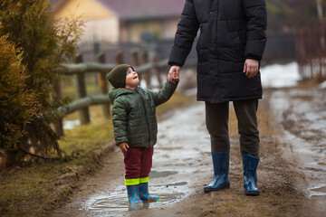 Father and son walking in the fresh air in rubber boots on the puddles and mud after the rain....