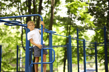 Obraz premium athlete boy in the park goes in for sports hung on his hands and does exercises on the uneven bars with his legs crossed