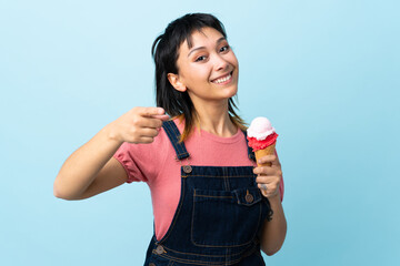 Young Uruguayan girl holding a cornet ice cream over isolated blue background points finger at you...