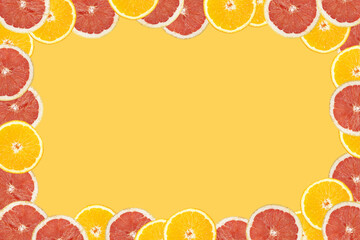 Orange and grapefruit cut in half on an seamless yellow background arranged around the frame, negative copy space