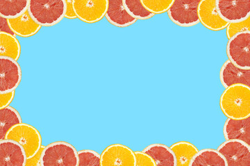 Orange and grapefruit cut in half on an seamless blue background arranged around the frame, negative copy space