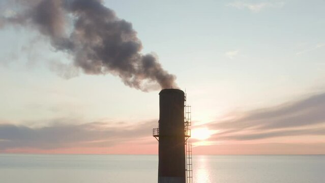 Evening sunset and blue sea Drone removes the chimney releases black smoke. The coal processing factory pollutes the environment with the release of toxic gases.