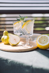Fresh lemonade with pear, lemon and mint leaves in beautiful glasses on the terrace on a hot summer day.