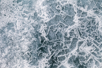 Structure of the ice surface in the spring. Top view of ice with bubbles and lines of cracks in March. Blue ice of Baikal lake. Cold winter abstract background. Flat lay, copy space, close-up, mock up