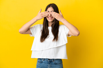Young caucasian woman isolated on yellow background covering eyes by hands and smiling