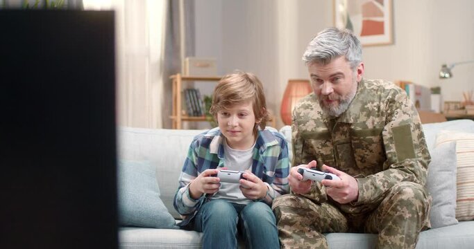 Happy military father playing video games with son at home