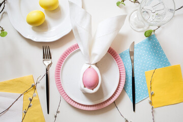 table setting for Easter. pastel dusty pink egg in napkin folded in shape of easter bunny