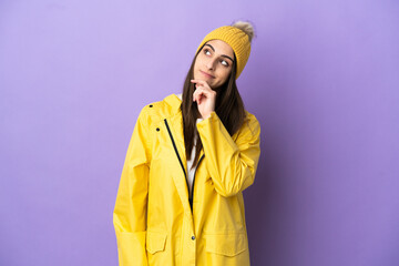 Young caucasian woman wearing a rainproof coat isolated on purple background and looking up