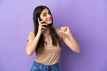 Young caucasian woman using mobile phone isolated on purple background proud and self-satisfied