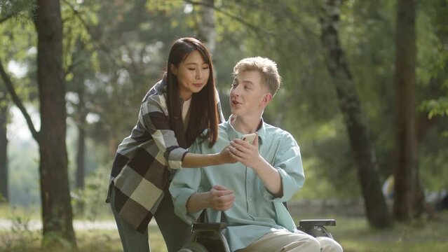 Being in the public park in a good weather, a young sweet couple decide calling their friends, they wave hands and smile