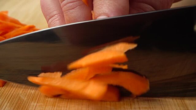 The cook cuts carrots with a knife. Slow motion.