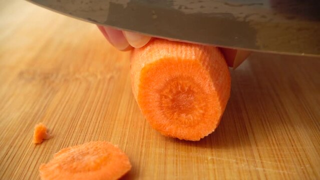 The cook cuts carrots with a knife. Slow motion.