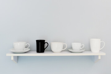 Five cups stand on a white shelf