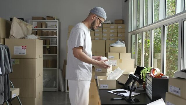 Asian man business owner working, packing the order for shipping to customer. Male entrepreneur packaging box for delivery in store warehouse.