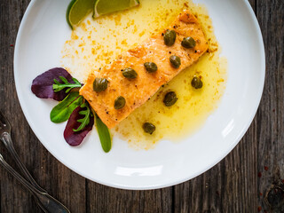 Butter sauce fried salmon steak with capers and lime  on wooden table
