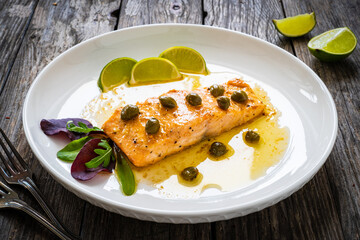 Butter sauce fried salmon steak with capers and lime  on wooden table
