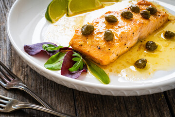 Butter sauce fried salmon steak with capers and lime  on wooden table
