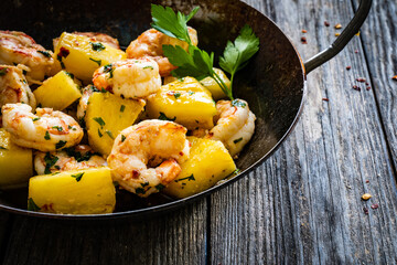 Fried prawns and pineapple in frying pan on wooden table
