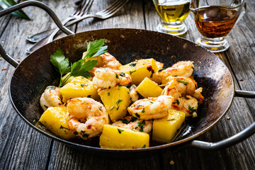 Fried prawns and pineapple in frying pan on wooden table
