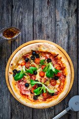 Circle prosciutto pizza with mozzarella, pork ham and black olives on wooden table
