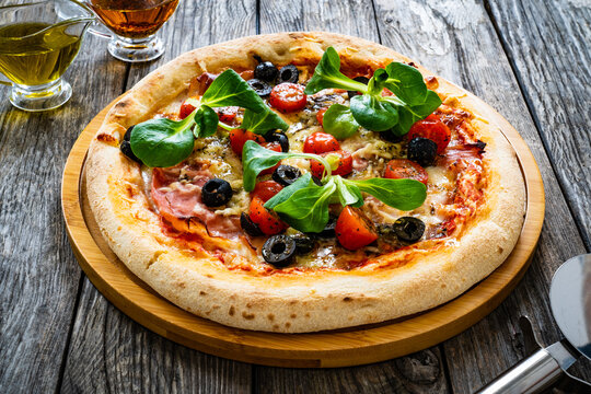 Circle prosciutto pizza with mozzarella, pork ham and black olives on wooden table
