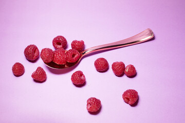 spoon with raspberries on lilac background
