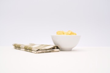 Natural potato chips in a white bowl with table napkin on a white surface against a white wall