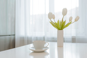 White tulips in a vase and a white cup on the table