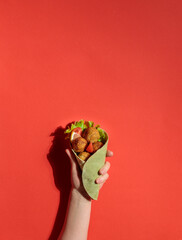 the hand holds pita bread with falafel or meatballs. On a red background, hard light
