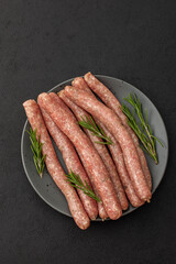 Raw pork sausages with rosemary in a plate close-up on a dark background