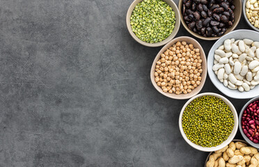 Different types of legumes in bowls, green peas and chickpeas , colored beans and maash and peanuts, top view, copy space