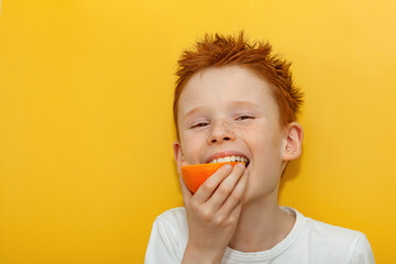 A red-haired boy appetizingly bites half of a juicy orange on a yellow background