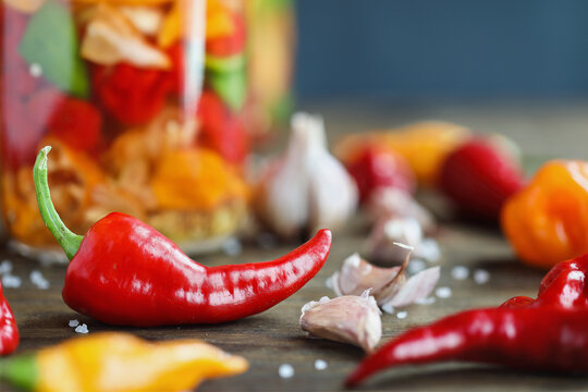 Cyklon pepper with variety of other spicy peppers and garlic cloves in front of a mason jar of fermenting hot sauce. Selective focus with blurred background and foreground.