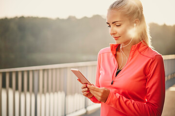 Fit young woman looking on mobile phone during morning running exercise