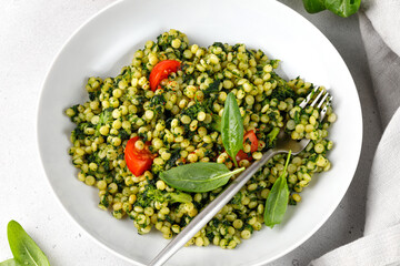 Dish with Ptitim pasta with spinach and broccoli, cherry tomatoes. Healthy homemade dinner. Grey background. Top view.