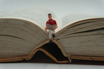 A miniature man sits and reads on an old book. World Book and Copyright Day.Reading books....