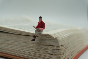A miniature man sits and reads on an old book. World Book and Copyright Day.Reading books....